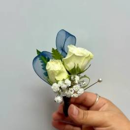 White rose boutonniere with blue ribbon loops and baby's breath