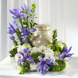 Purple irises and white daisies arranged around a decorative urn.