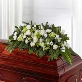 White and green floral casket spray on a polished wooden casket