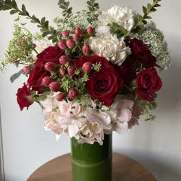 Bouquet of red roses, white carnations, and pink berries in a green glass vase