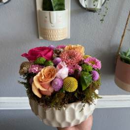 Compact bouquet of pink, peach, and yellow flowers in a white ceramic bowl