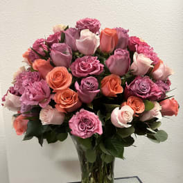Bouquet of pink, lavender, and coral roses in a clear glass vase