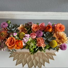 Low rectangular arrangement of orange and pink flowers with succulents