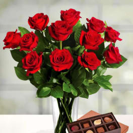 Red roses in a clear vase with a box of chocolates