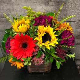 Bright mixed arrangement with sunflowers and red gerbera daisies in a rustic square container