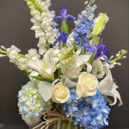 Tall arrangement of white roses, lilies, and blue hydrangeas in a clear glass vase