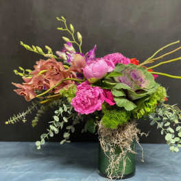 Asymmetrical arrangement with pink peonies, peach orchids, and green accents in a glass cylinder vase