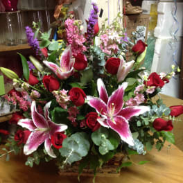 Basket arrangement of red roses and pink lilies with purple accents
