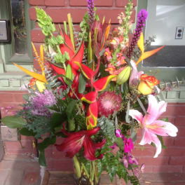 Tall tropical bouquet with lilies, calla lilies, and protea in a glass vase
