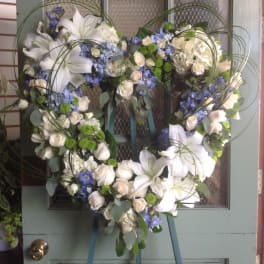 Heart-shaped floral wreath with white lilies, roses, and blue flowers on an easel