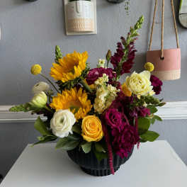 Mixed bouquet with sunflowers, roses, and snapdragons in a black vase