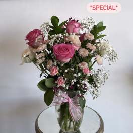 Pink roses and small white flowers in a clear glass vase with a pink ribbon
