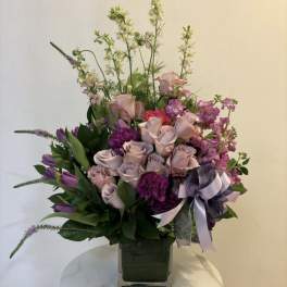 Lavender and pink floral arrangement in a square glass vase with a ribbon