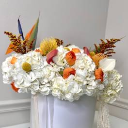 White floral arrangement with orange accents in a round white box