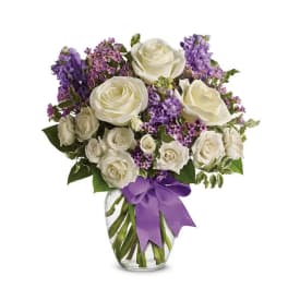 White roses and purple flowers in a clear glass vase with a purple ribbon