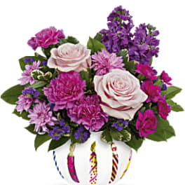 Pink and purple flower arrangement in a white vase with candle designs