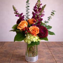 Orange roses and purple flowers in a clear glass vase