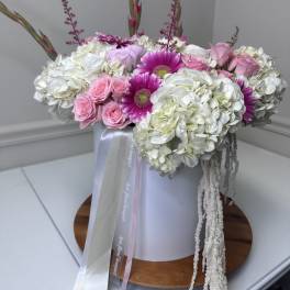 Pink roses and magenta daisies arranged with white hydrangeas in a box