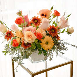 Mixed bouquet of peach, coral, and white flowers in a clear glass vase