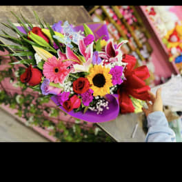 Mixed bouquet with roses, lilies, gerbera daisies, and a sunflower in purple wrap