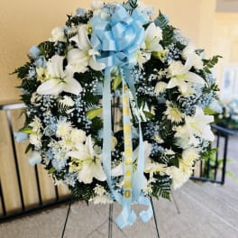 White lily and blue floral funeral wreath with a blue bow