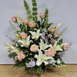 Large floral arrangement with white lilies, peach roses, and purple accents in a basket
