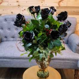 Black roses arranged in a glass vase with greenery