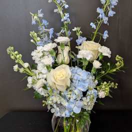 White roses and blue flowers arranged in a glass vase
