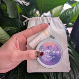 Hand holding a lavender haze lip balm and a champagne lip balm in a small pouch