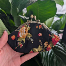 Floral-print fabric coin purse with a metal clasp held in a hand