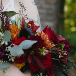 Bride holding a bouquet of red, orange, and burgundy flowers