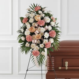Standing spray of peach roses, pink carnations, and white daisies on an easel beside a casket