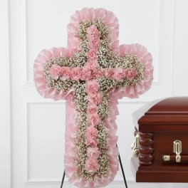 Pink floral cross standing beside a wooden casket