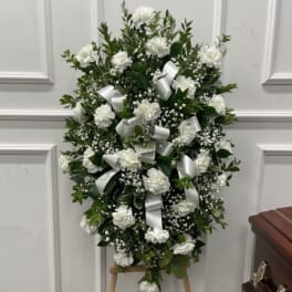 Standing spray of white carnations and baby's breath with white ribbon bows on a wooden easel.