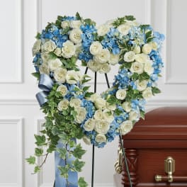 Heart-shaped floral wreath with white roses and blue hydrangeas on a stand