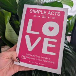 Hand holding a pink book cover reading "Simple Acts of Love"