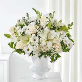 White floral arrangement in a white vase with roses, lilies, and daisies