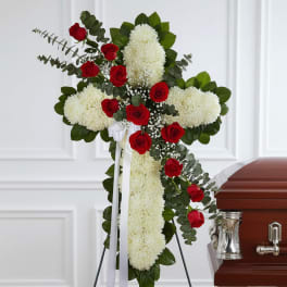 Red roses and white flowers arranged on a standing cross beside a casket