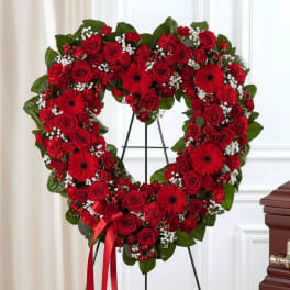 Heart-shaped red rose and gerbera wreath on an easel with a ribbon