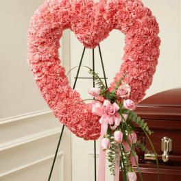 Pink heart-shaped floral wreath on an easel beside a casket