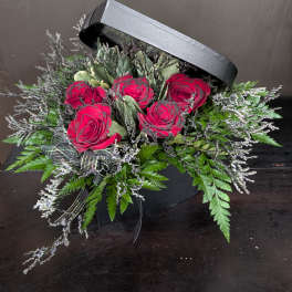 Red roses in a black hatbox with greenery and ribbon
