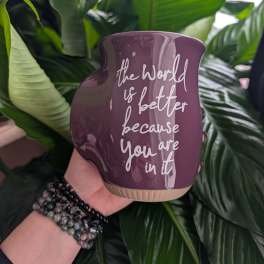 Purple ceramic planter with white text held in front of large green leaves