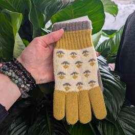 Hand holding a pair of patterned knit gloves in front of large green leaves