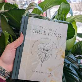 Hand holding a book in front of large green leaves