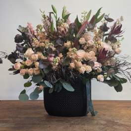 Large arrangement of blush roses and dark foliage in a black container