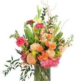 Tall mixed arrangement of peach roses, pink flowers, and yellow accents in a clear glass vase