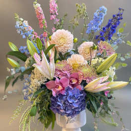 Mixed bouquet of pastel and blue flowers in a white pedestal vase