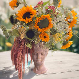 Sunflower arrangement in a sculpted face vase with trailing burgundy amaranthus