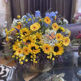 Mixed bouquet of yellow sunflowers and gerbera daisies in a gold vase