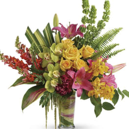 Mixed bouquet of yellow roses, pink lilies, and orchids in a glass vase